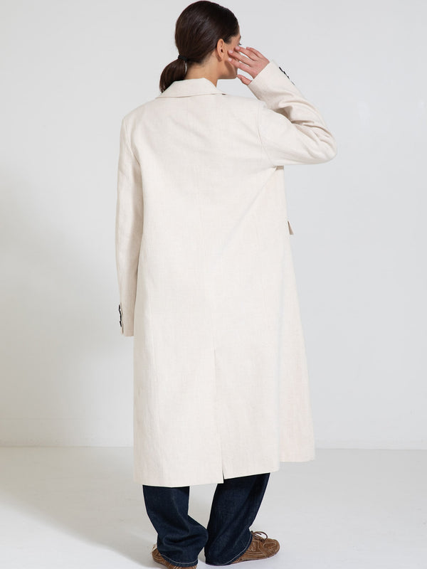 A woman in a long, light beige coat with a relaxed fit, styled with dark jeans, showcasing a minimalist look by MEOTINE.