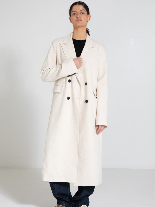 A model wearing a stylish cream-colored MEOTINE coat with a double-breasted design, paired with dark jeans against a neutral backdrop.