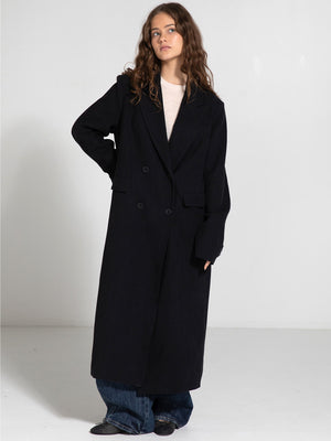 A model poses in a stylish black MEOTINE coat, featuring a double-breasted design, paired with loose denim pants.