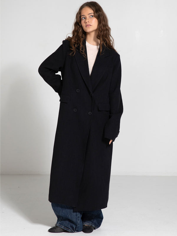 A model poses in a stylish black MEOTINE coat, featuring a double-breasted design, paired with loose denim pants.