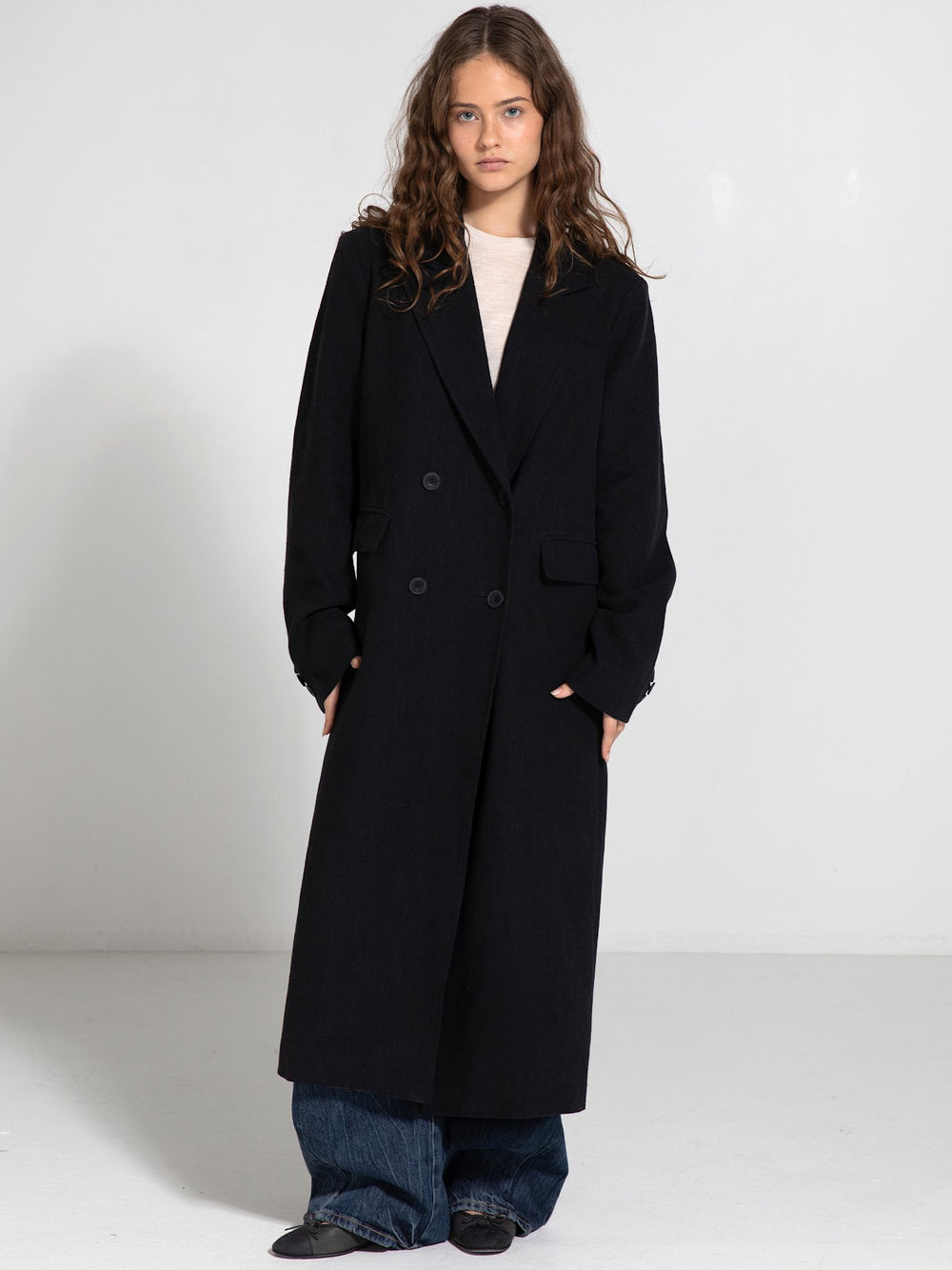A model wearing a long black double-breasted coat paired with wide-leg jeans, showcasing MEOTINE's stylish outerwear.