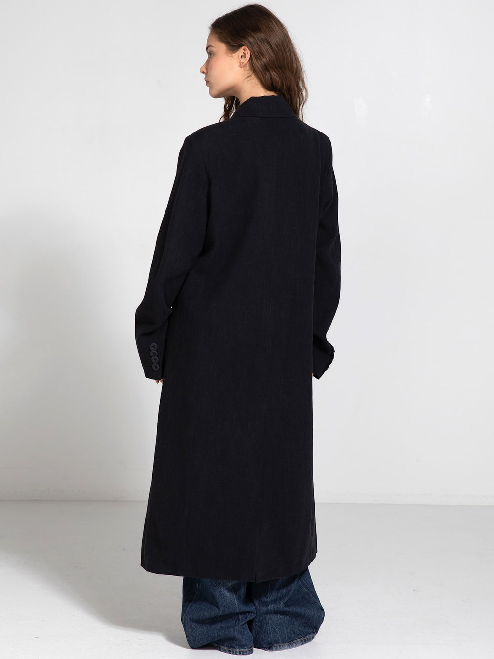 A model wearing a long black double-breasted coat paired with wide-leg jeans, showcasing MEOTINE's stylish outerwear.