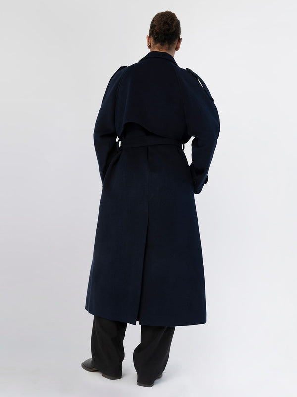 A model wearing a stylish navy coat from MEOTINE, showcasing a unique back design and relaxed fit, paired with black pants.