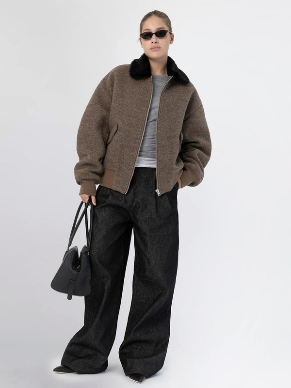 Stylish model wearing a brown bomber jacket with a black fur collar, paired with wide-leg jeans and sunglasses, showcasing MEOTINE fashion.