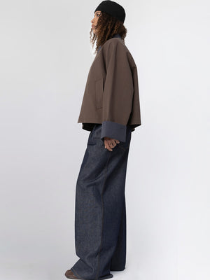 A model showcases a stylish brown oversized jacket with contrasting blue cuffs, paired with wide-leg denim pants, embodying MEOTINE's modern aesthetic.