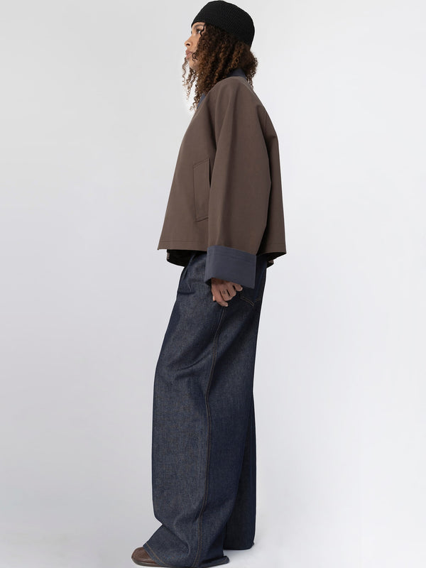 A model showcases a stylish brown oversized jacket with contrasting blue cuffs, paired with wide-leg denim pants, embodying MEOTINE's modern aesthetic.