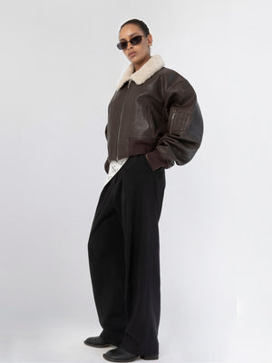 Stylish model wearing a brown bomber jacket with a shearling collar, paired with wide-leg black trousers. MEOTINE brand.