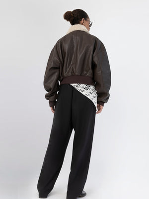 A model showcases a stylish brown leather bomber jacket with a cozy shearling collar, paired with loose black trousers. MEOTINE.