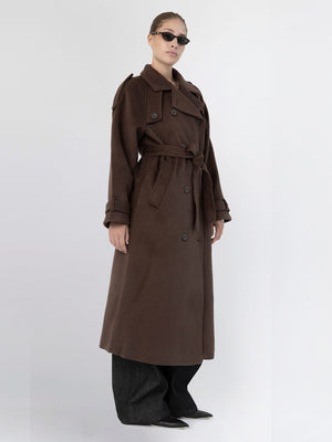 A model showcases a stylish brown trench coat with a belt, paired with oversized black pants and sunglasses, representing MEOTINE's chic aesthetic.