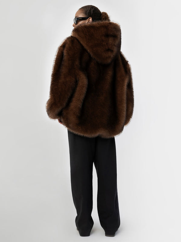 A model wearing a luxurious brown faux fur coat with a hood, paired with black wide-leg pants, showcasing MEOTINE's elegant style.