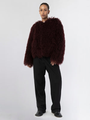 A model wears a plush, burgundy faux fur jacket paired with black wide-leg trousers, showcasing MEOTINE's cozy style.