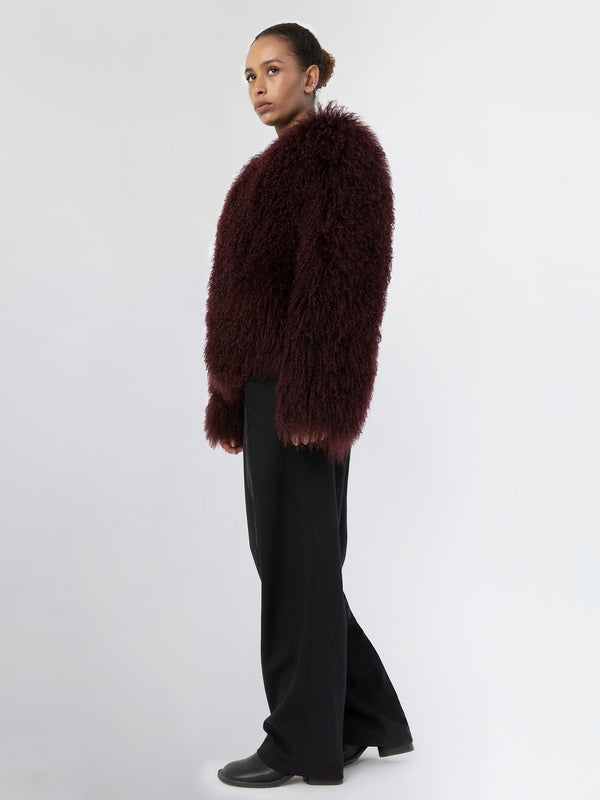 A model showcases a plush, burgundy MEOTINE sweater with a fluffy texture, paired with black trousers for a chic look.