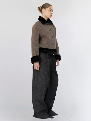 A model showcases a stylish brown cropped jacket with a black fur collar, paired with wide-leg dark trousers by MEOTINE.