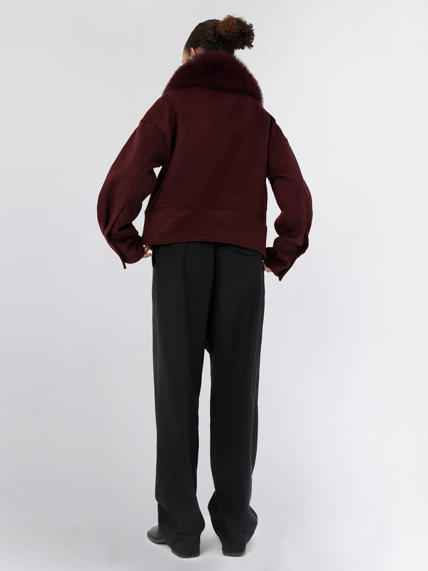 A model showcases a burgundy oversized jacket with a plush fur collar, paired with black wide-leg trousers, embodying MEOTINE's chic style.