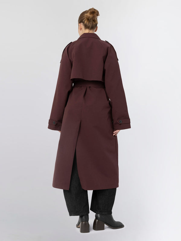 A model showcases a stylish burgundy trench coat with a cropped design and a back slit, paired with wide-leg pants. MEOTINE.