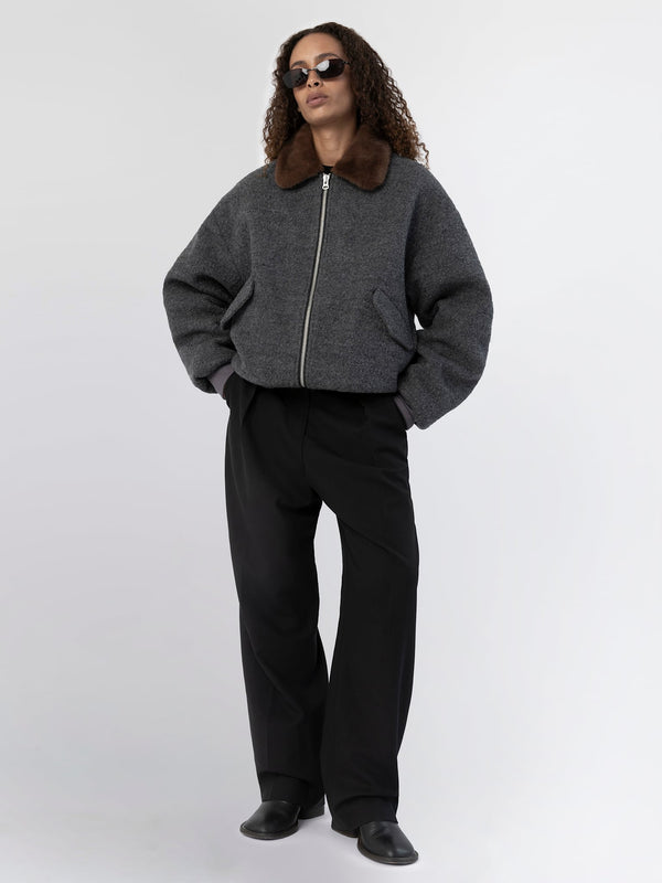 Stylish model wearing a gray cropped jacket with a brown fur collar, paired with black wide-leg trousers and sunglasses. MEOTINE.