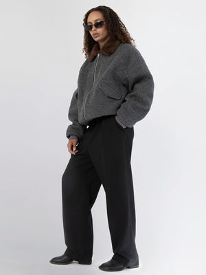 A model showcases a stylish gray bomber jacket with a fur collar, paired with wide-leg black trousers and sunglasses, representing MEOTINE.