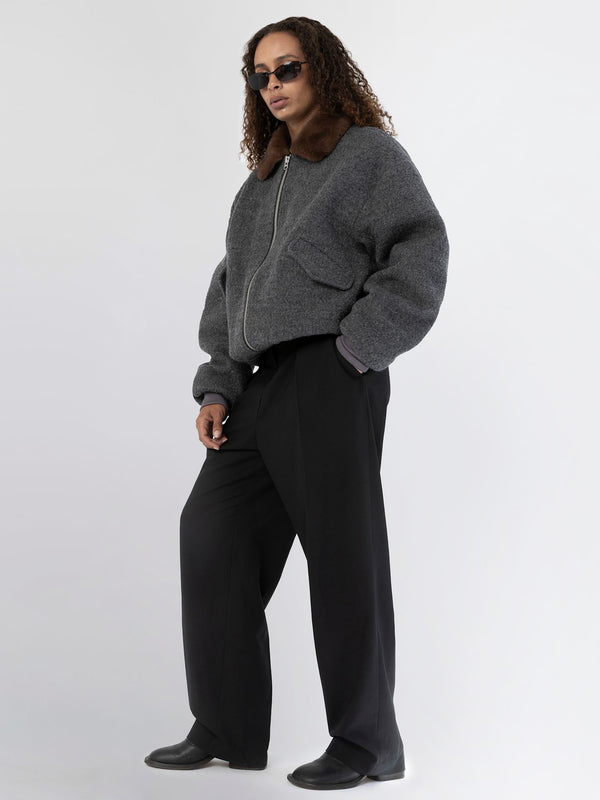 A model showcases a stylish gray bomber jacket with a fur collar, paired with wide-leg black trousers and sunglasses, representing MEOTINE.
