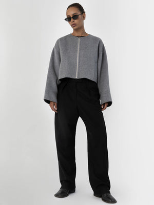 A model wears a cropped gray jacket with a zip and wide black trousers, showcasing a modern, stylish look by MEOTINE.