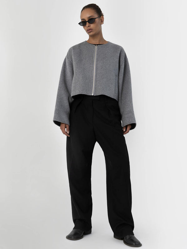 A model wears a cropped gray jacket with a zip and wide black trousers, showcasing a modern, stylish look by MEOTINE.