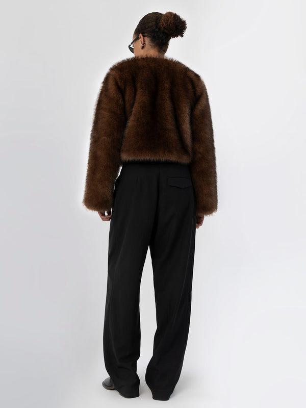 A model wearing a brown faux fur jacket and black wide-leg trousers, showcasing a stylish and cozy look by MEOTINE.