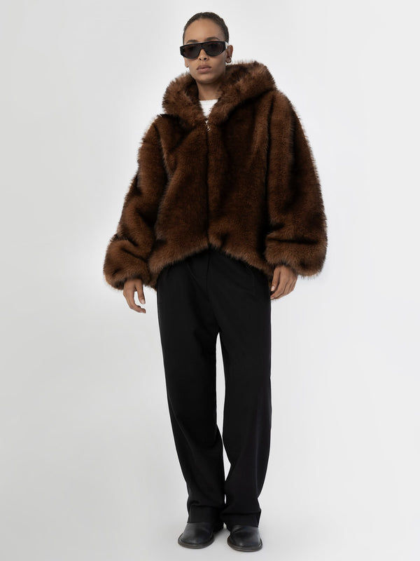 A model wears a luxurious brown faux fur jacket with a hood, paired with black trousers and sunglasses, showcasing MEOTINE's style.