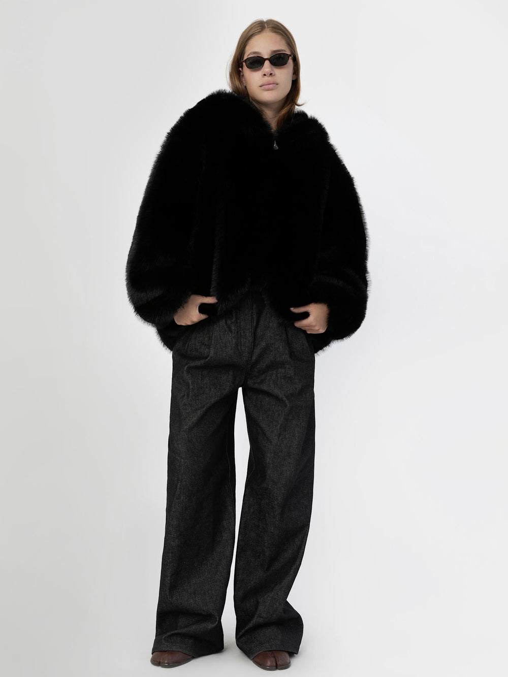 A model showcases a luxurious black faux fur coat by MEOTINE, paired with stylish sunglasses and knee-high brown boots.