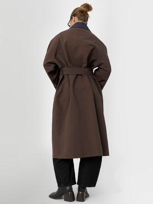 A model wearing a brown MEOTINE trench coat with a belted waist, paired with dark wide-leg pants, viewed from the back.