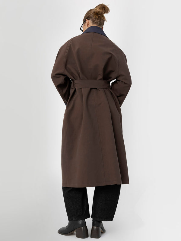 A model wearing a brown MEOTINE trench coat with a belted waist, paired with dark wide-leg pants, viewed from the back.