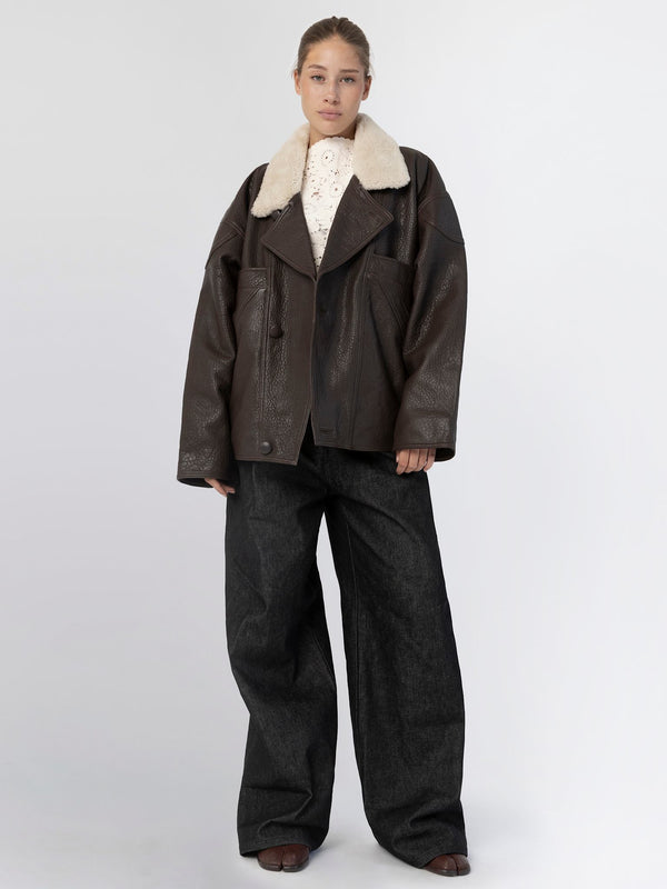 A model showcases a stylish brown leather jacket with a plush collar, paired with wide-leg dark jeans, embodying MEOTINE's chic aesthetic.