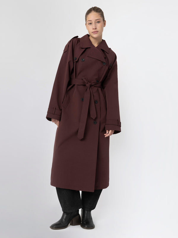 A model showcases a stylish burgundy trench coat with a belted waist, featuring a classic double-breasted design by MEOTINE.