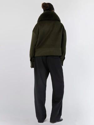 A model wearing a dark green oversized sweatshirt with a fur collar, paired with loose black trousers, showcasing MEOTINE's style.