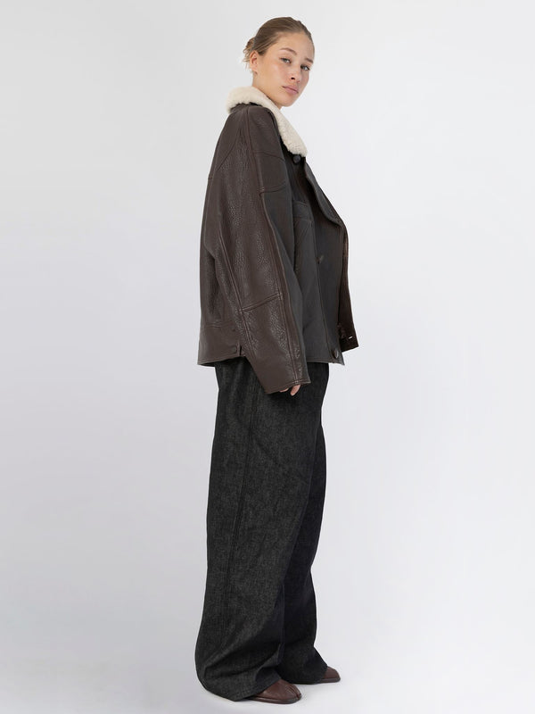 A model showcases a stylish brown leather jacket with a cozy white collar, paired with loose black trousers, embodying MEOTINE's chic aesthetic.