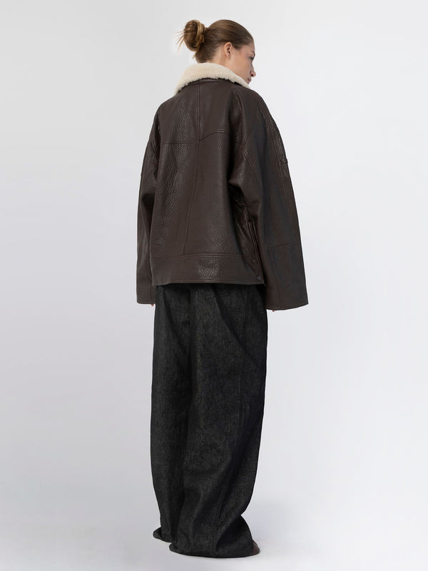 A model showcases a stylish brown leather jacket with a cozy fur collar, paired with loose-fitting dark trousers by MEOTINE.