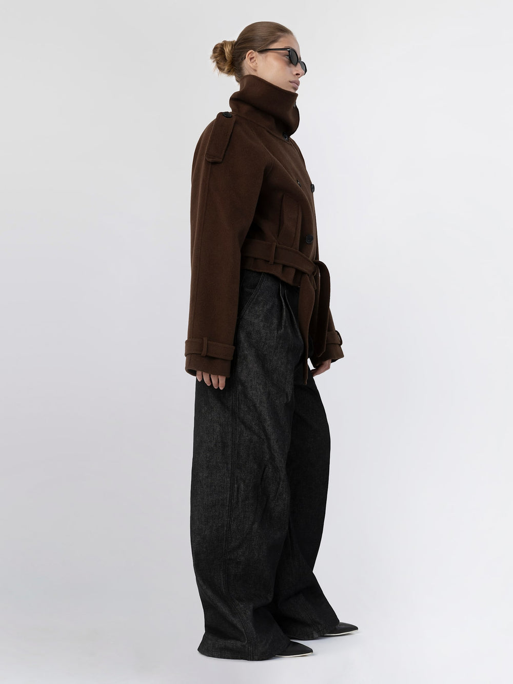 A model showcases a stylish brown double-breasted coat with a high collar and belted waist, complemented by sleek sunglasses. MEOTINE.