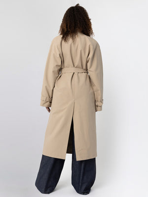 A model wearing a beige trench coat with a back slit, paired with wide-leg denim pants, showcasing MEOTINE's stylish design.