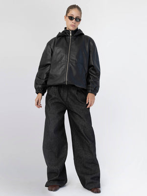 A model showcases a stylish black leather jacket paired with oversized dark denim pants, embodying a chic urban look by MEOTINE.