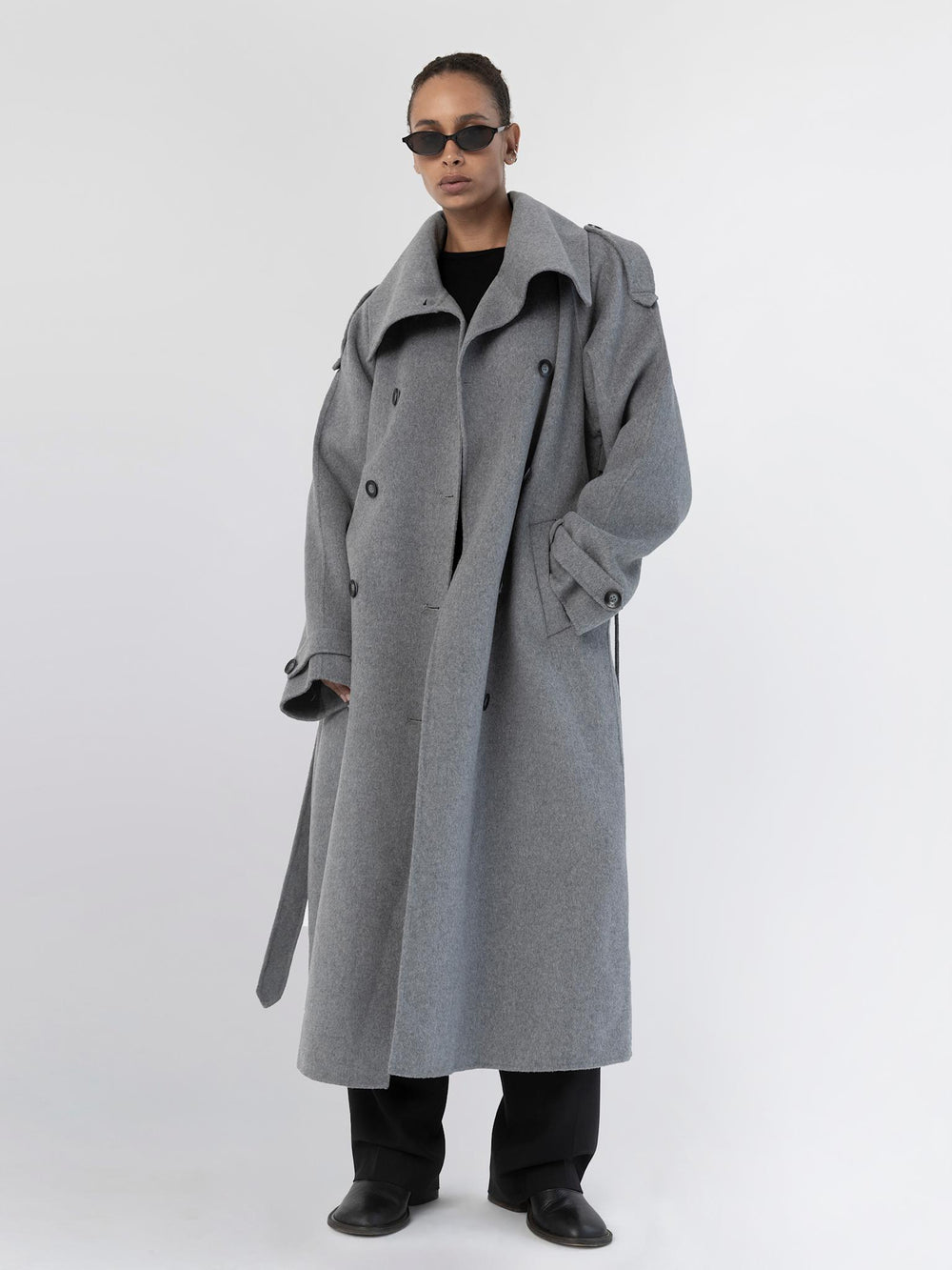 A model showcases a stylish gray oversized coat with a dramatic collar, paired with sleek black attire and sunglasses, by MEOTINE.