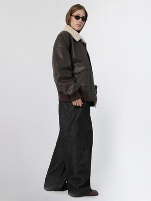 A model showcases a brown leather jacket with a shearling collar, paired with wide-leg dark jeans, embodying MEOTINE's stylish aesthetic.