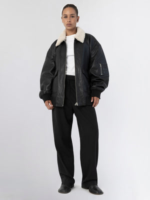 A model wears a black leather bomber jacket with a cozy shearling collar, paired with loose black trousers, showcasing MEOTINE's style.