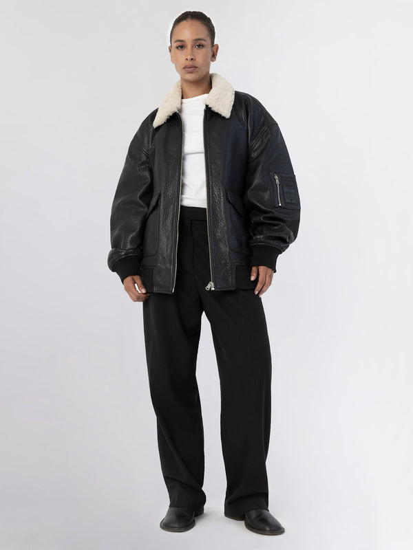 A model wears a black leather bomber jacket with a cozy shearling collar, paired with loose black trousers, showcasing MEOTINE's style.