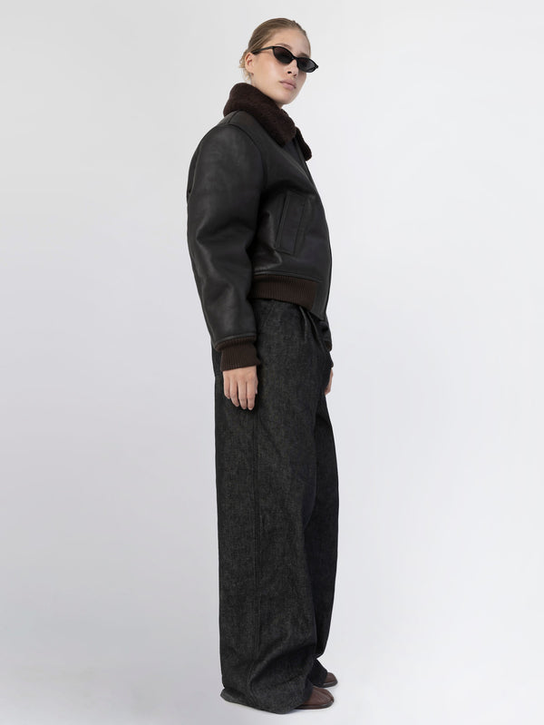 A model showcases a stylish black leather bomber jacket with a fur collar, paired with wide-leg dark trousers, representing MEOTINE's chic aesthetic.