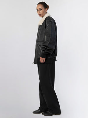 A model showcases a stylish black leather jacket with a cozy fur collar, paired with loose black trousers, embodying MEOTINE's chic aesthetic.