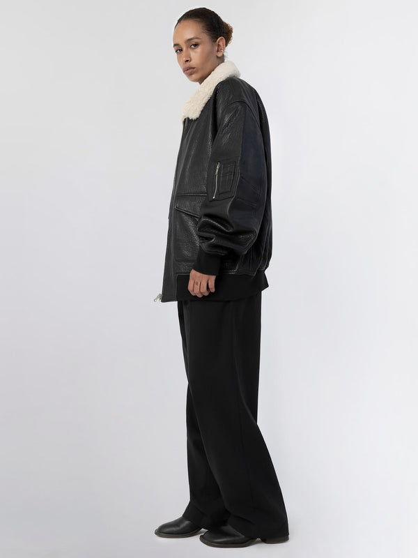 A model showcases a stylish black leather jacket with a cozy fur collar, paired with loose black trousers, embodying MEOTINE's chic aesthetic.