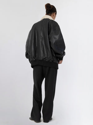 A model wearing a black oversized leather jacket with a fur collar, paired with loose black trousers, showcasing MEOTINE's style.