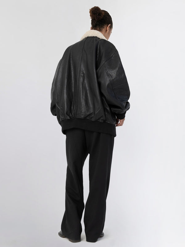A model wearing a black oversized leather jacket with a fur collar, paired with loose black trousers, showcasing MEOTINE's style.