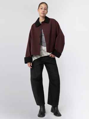A model wears a burgundy oversized jacket with a black collar, layered over a light top and paired with wide black pants. MEOTINE.