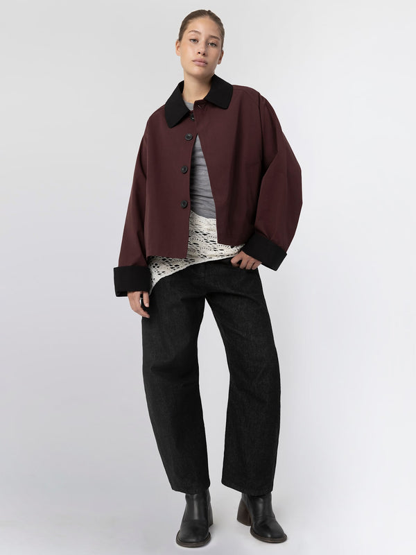 A model wears a burgundy oversized jacket with a black collar, layered over a light top and paired with wide black pants. MEOTINE.