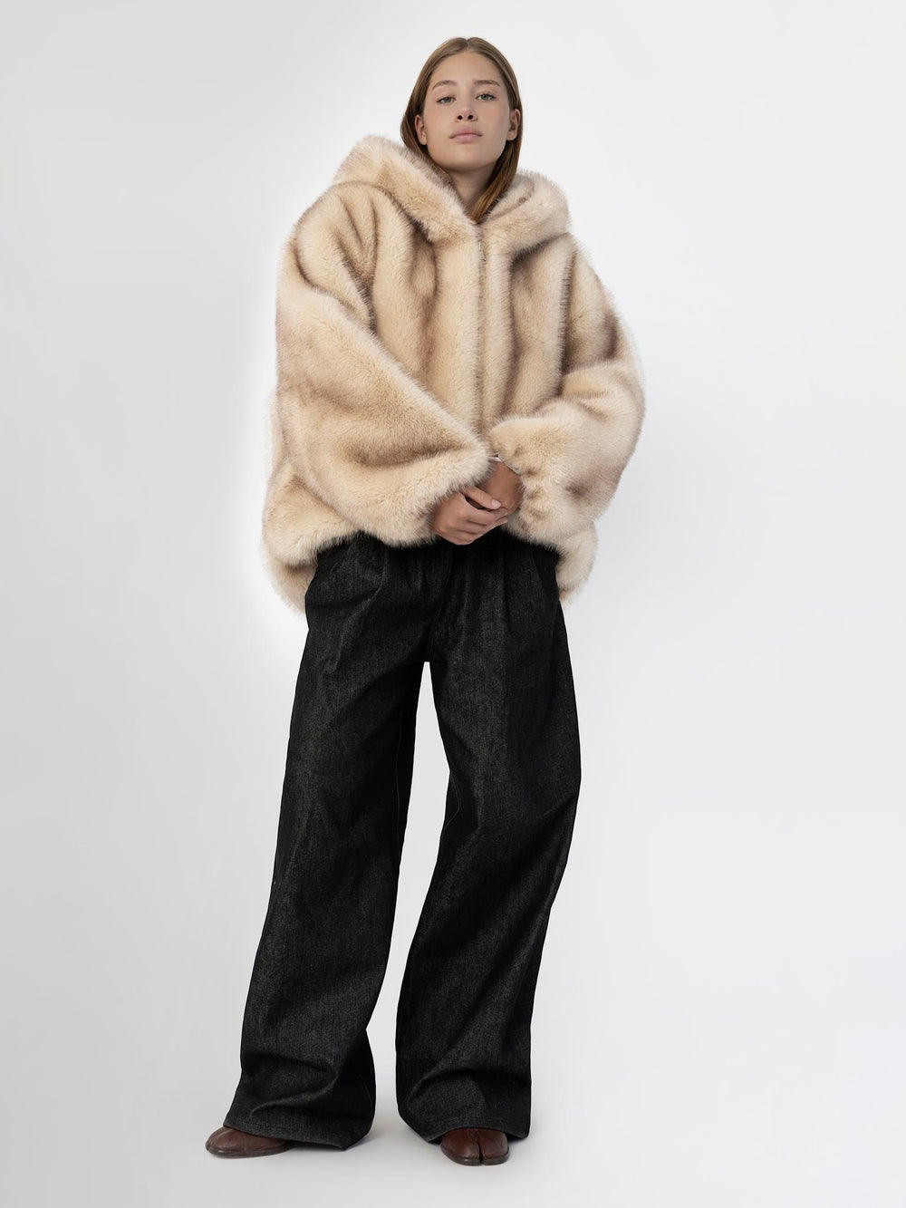 A model showcases a cozy, oversized beige fur jacket from MEOTINE, paired with a dark top and relaxed pants against a minimalist backdrop.
