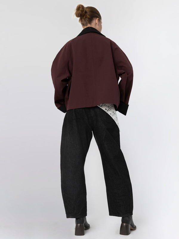 A model wearing a maroon oversized jacket paired with black wide-leg pants, showcasing a stylish and modern look by MEOTINE.